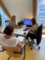 Mag. Elisabeth Schlögl, BA vom Museumsforum Steiermark schult zwei Mitarbeitende des Museums Kapfenberg, die vor ihrem Computer sitzen, in die PantherWeb-Datenbank ein. 